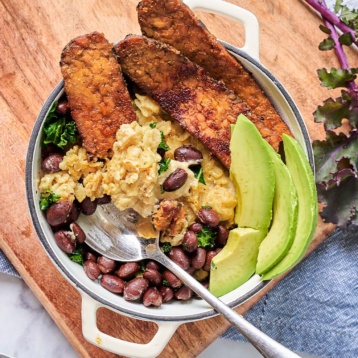 a bowl of oats topped with beans, kale, avocado and fried tempeh