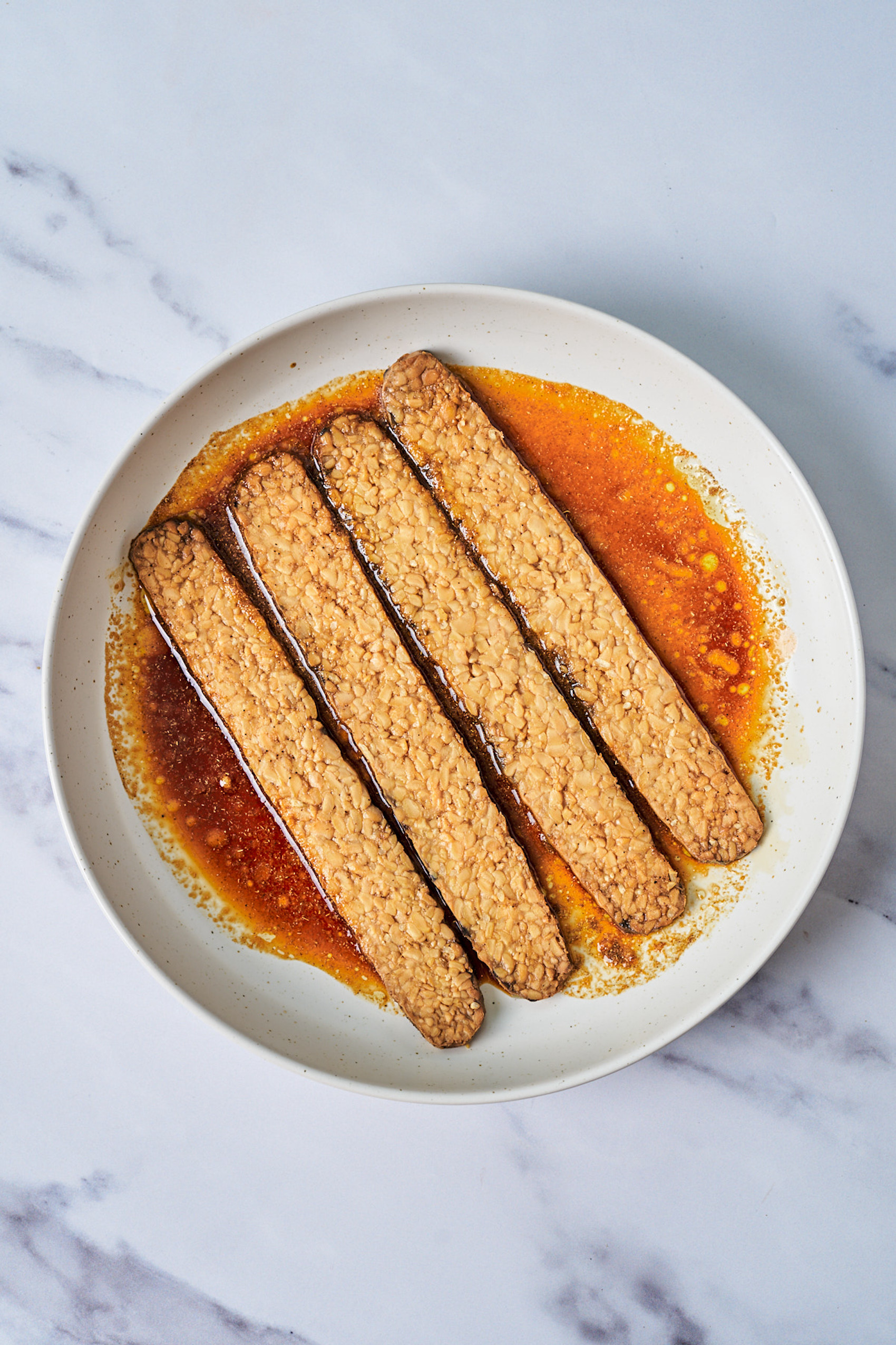 a bowl of sliced tempeh in a bowl of smoky bacon marinade