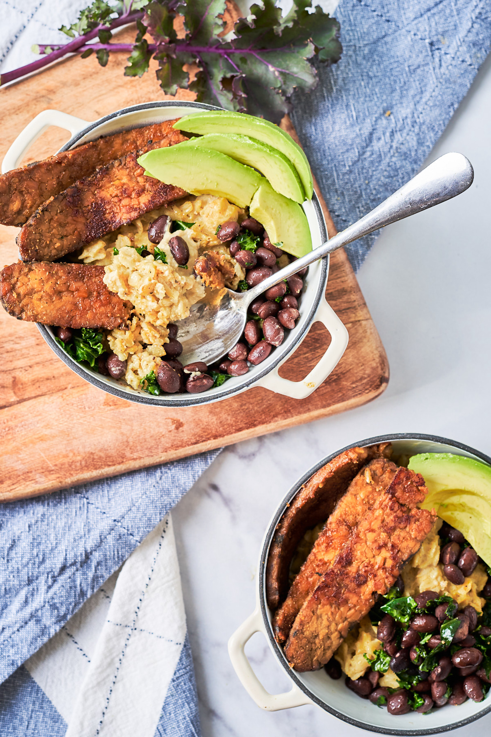 two bowls of oatmeal, each topped with fried tempeh, avocado and beans