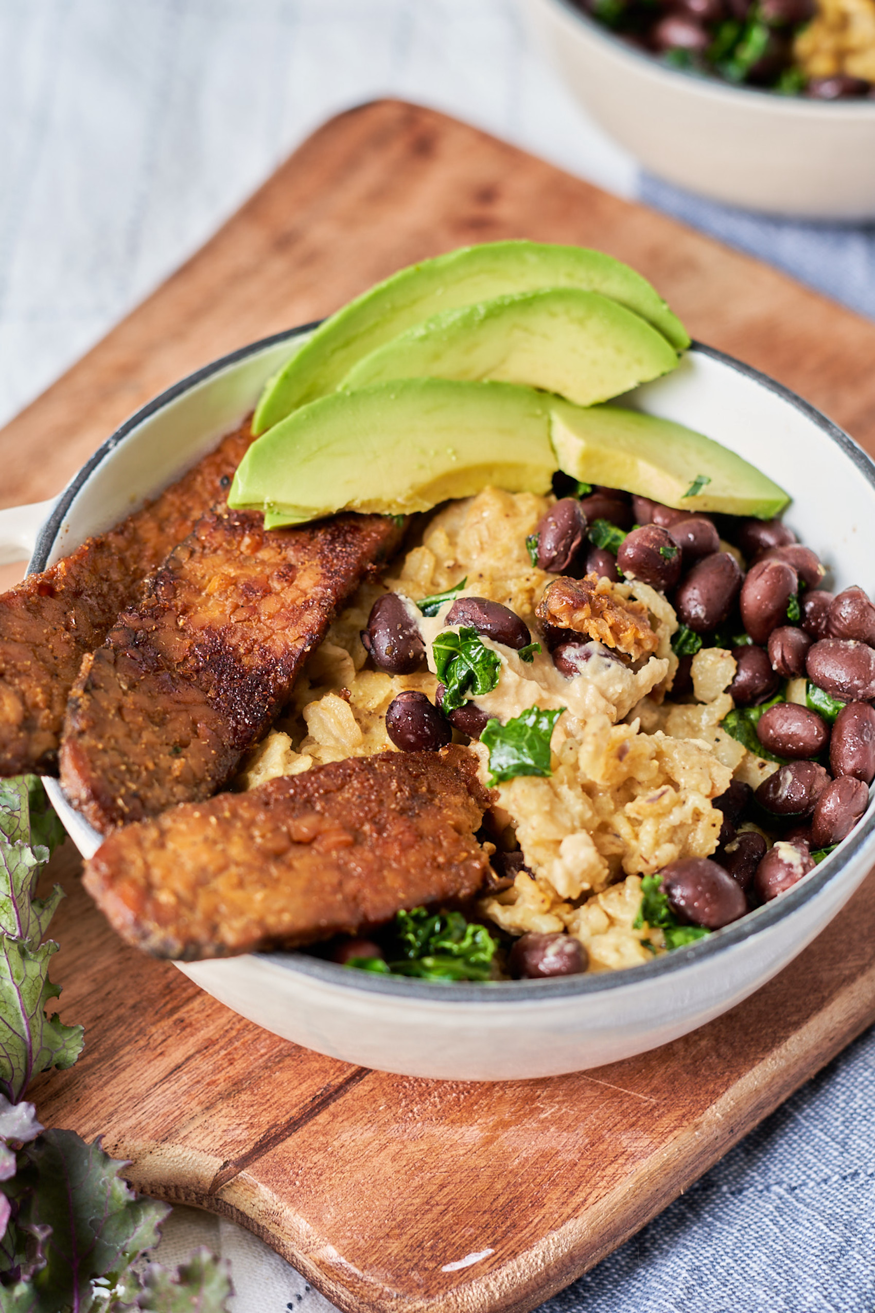 a bowl of oats topped with sliced avocado, sliced tempeh bacon and black beans