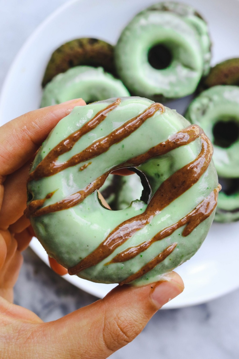 hand holding green frosted donut with chocolate stripes