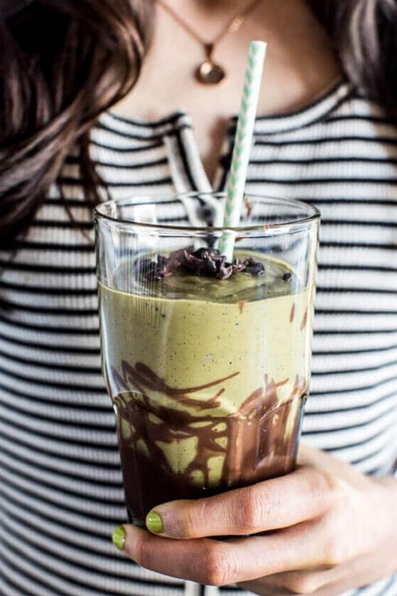 glass full of green smoothie with chocolate drizzle and a straw