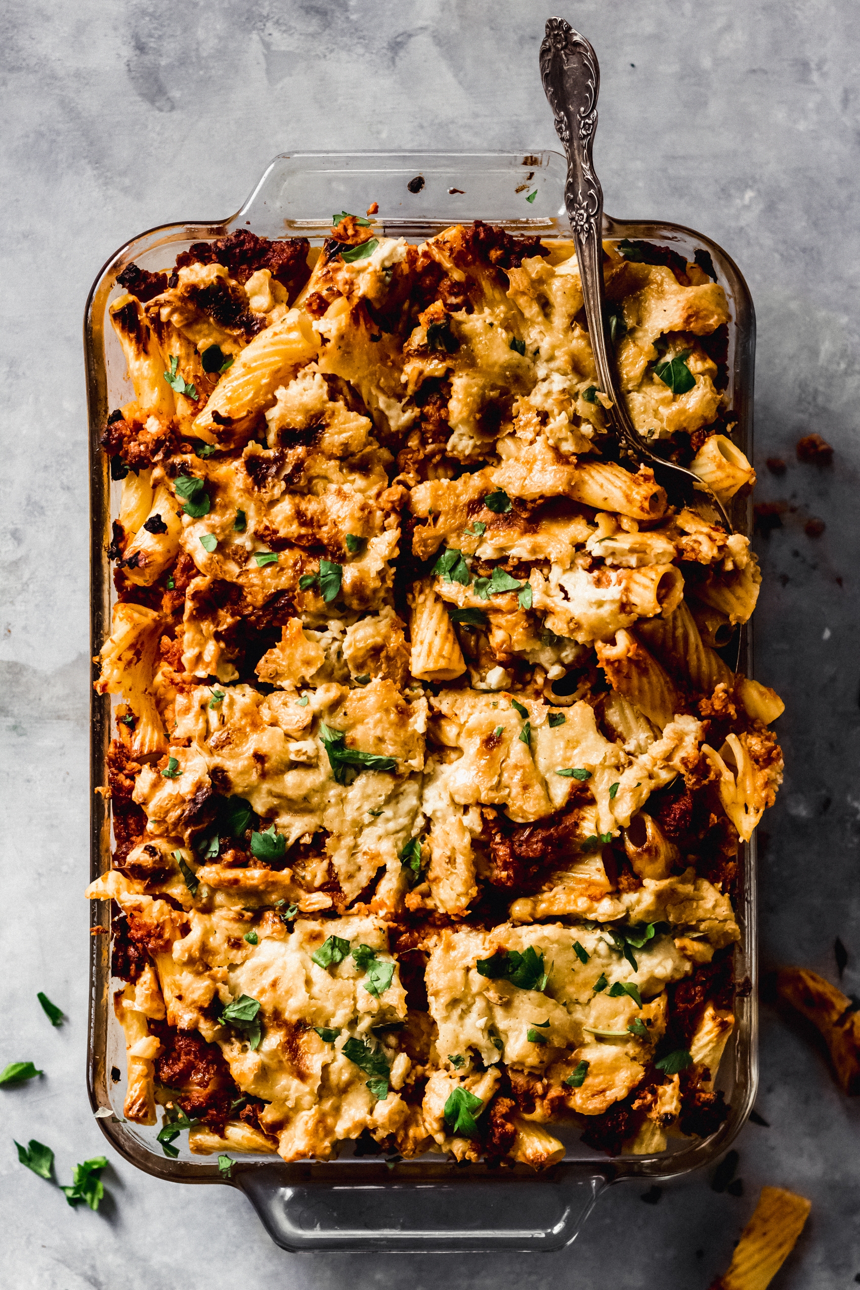 a spoon cutting into a casserole dish filled with baked pasta