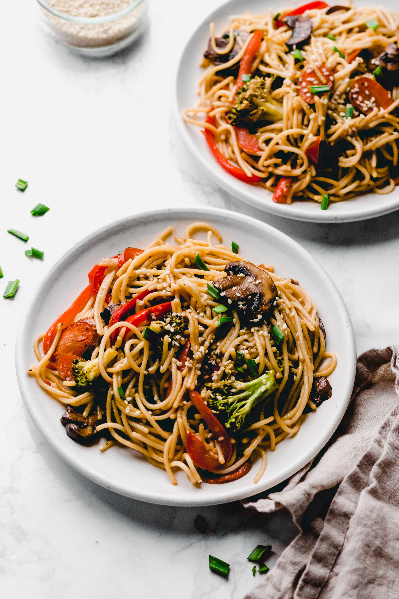 two plates of lo mein with mushrooms, peppers, carrots and broccoli