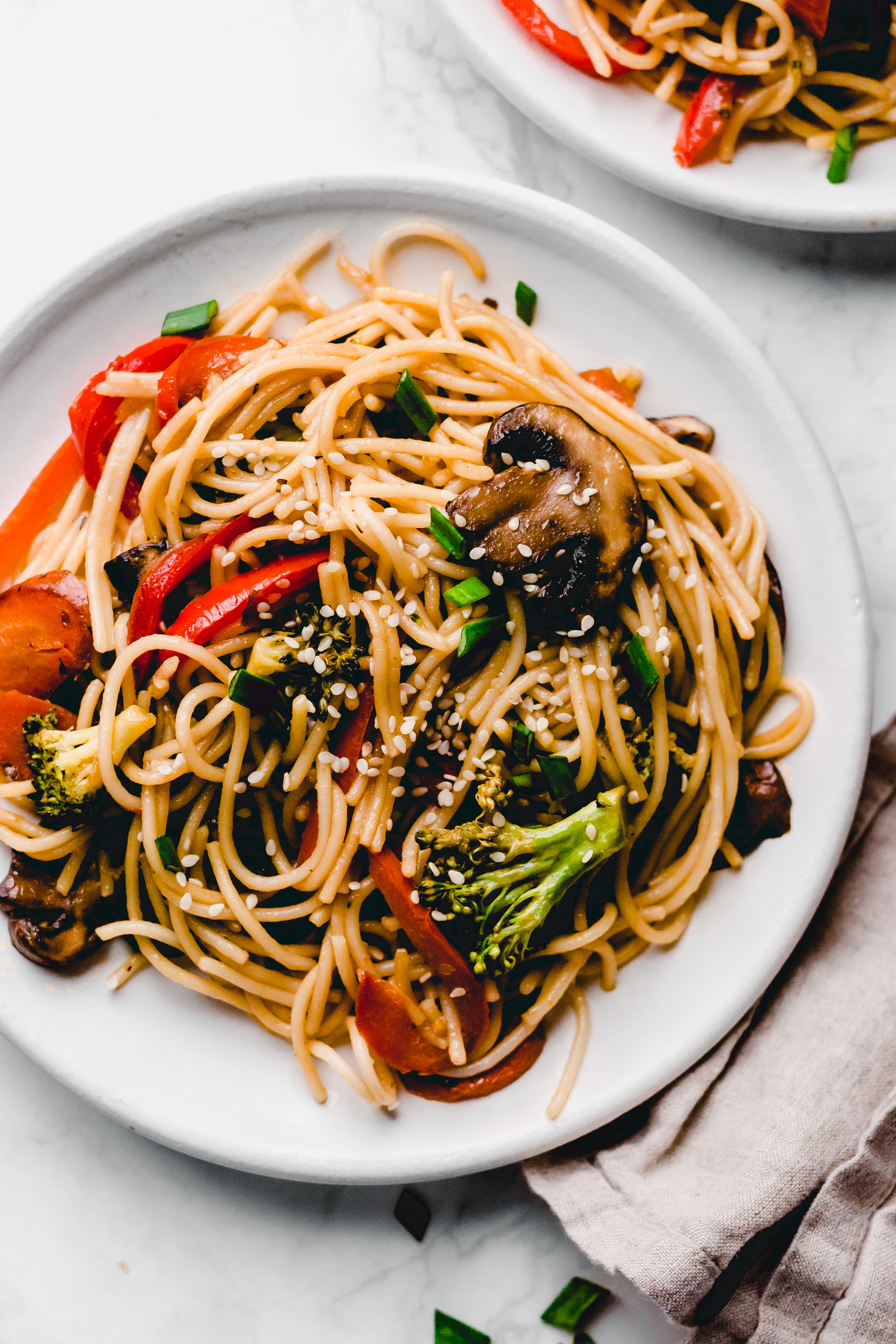 a close up of a plate of veggie lo main topped with white sesame seeds