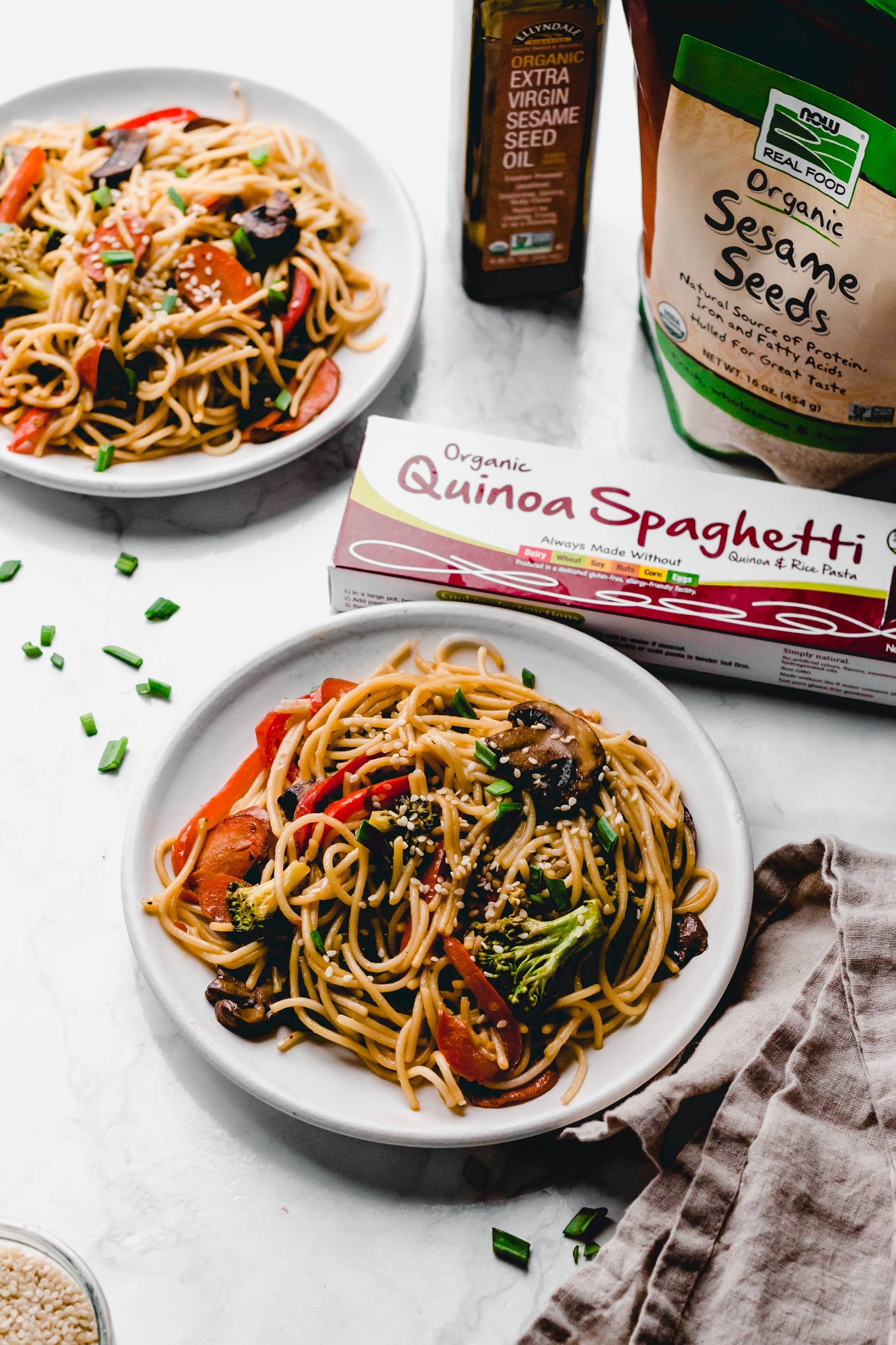 two plates of lo mein next to a box of gluten free spaghetti