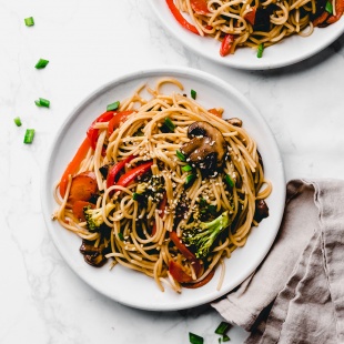 two plates of vegan lo mein topped with green onion and sesame seeds