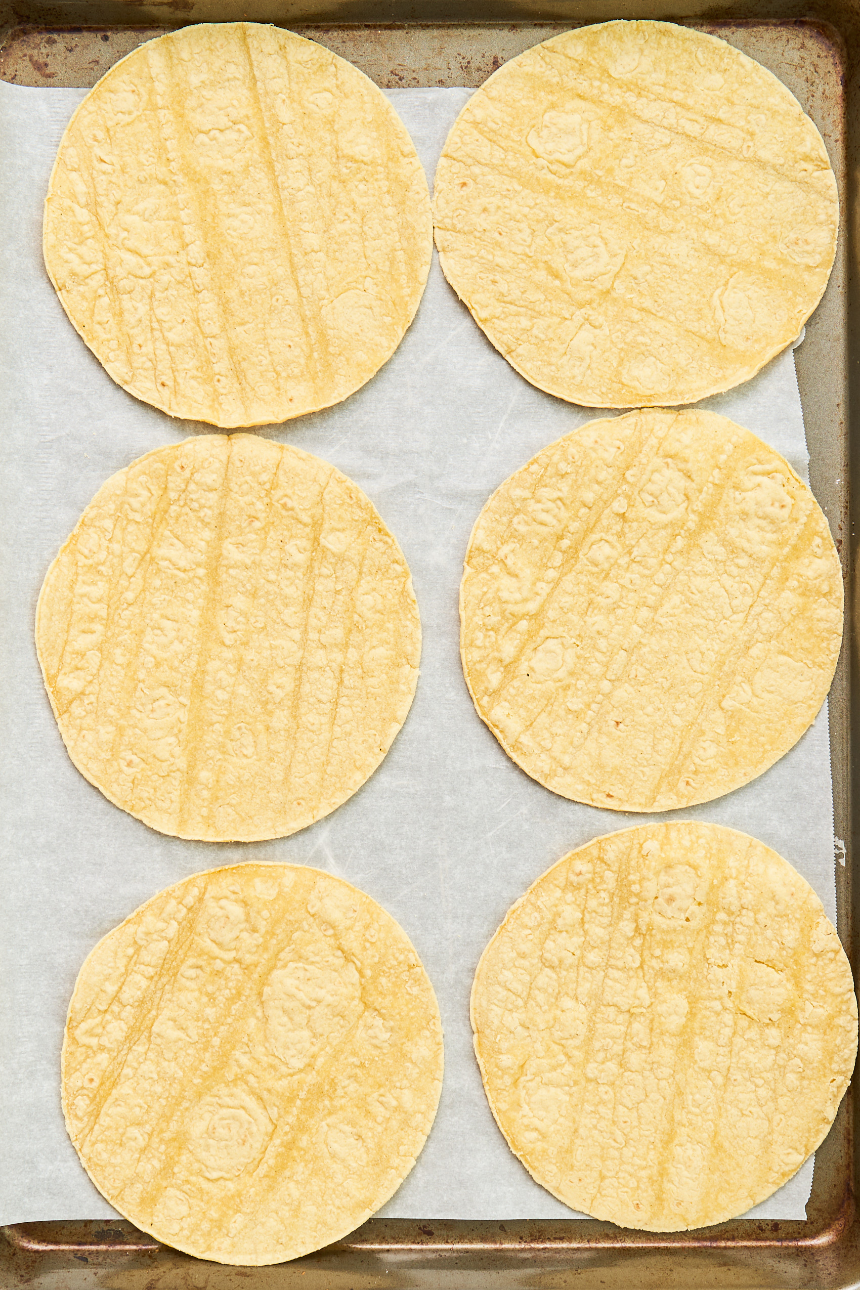 six corn tortillas arranged on a sheet tray lined with parchment paper