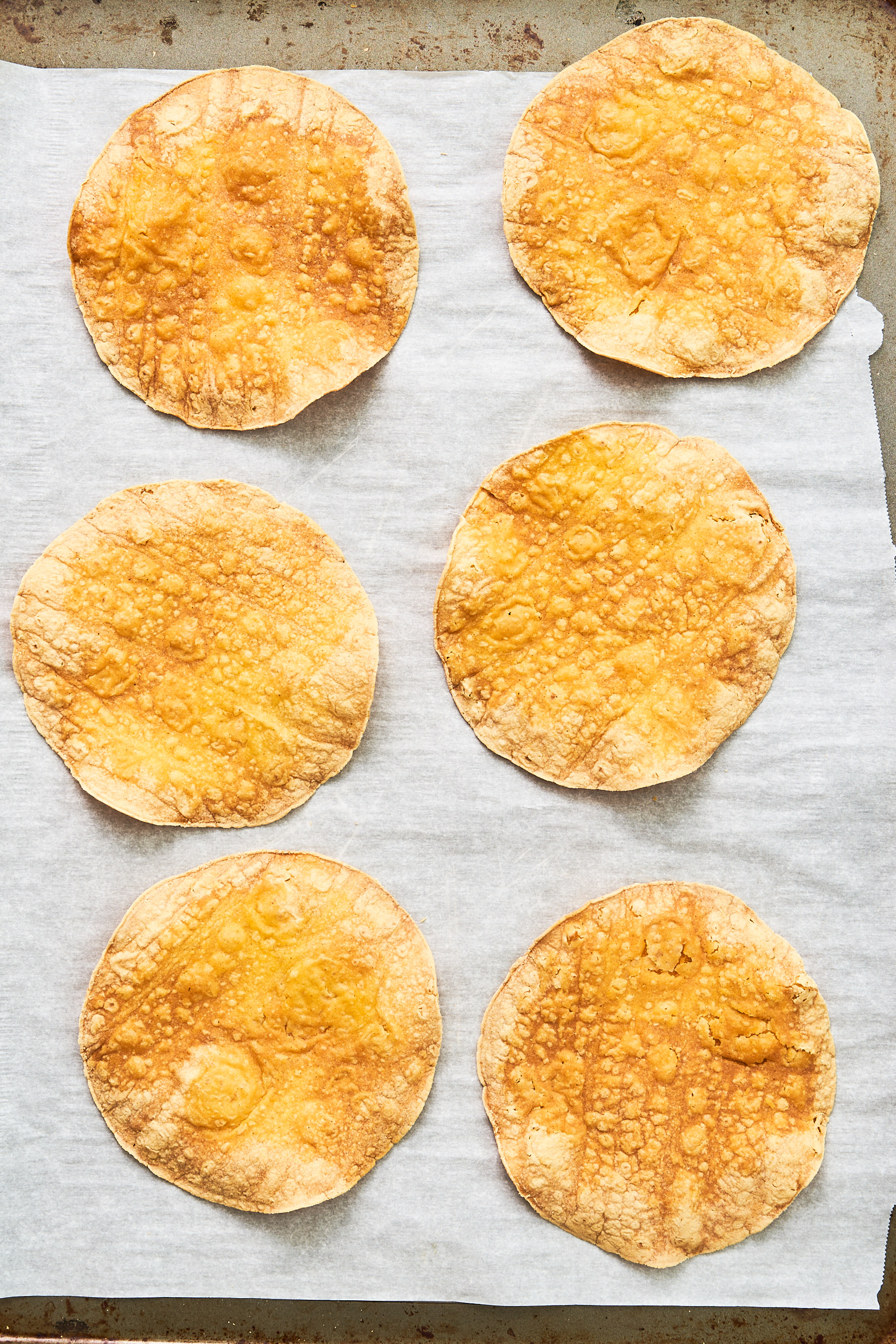 six corn tostadas on a pan lined with parchment paper