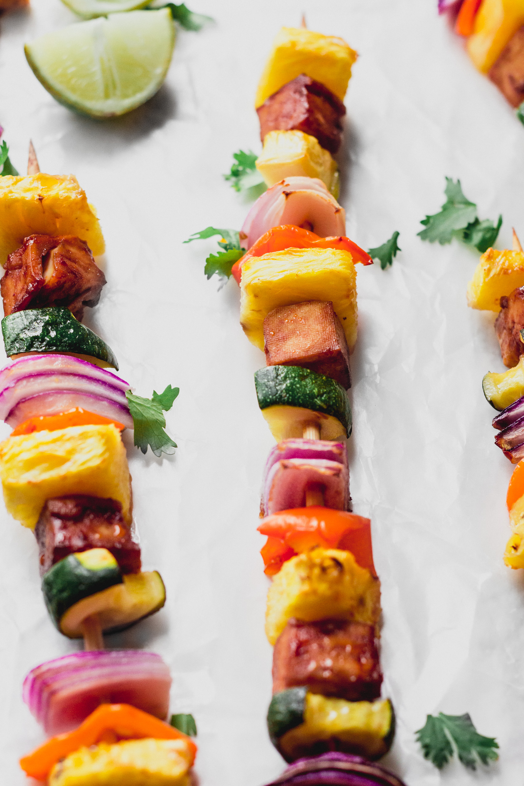 a close up shot of three vegetable skewers surrounded by scattered herbs