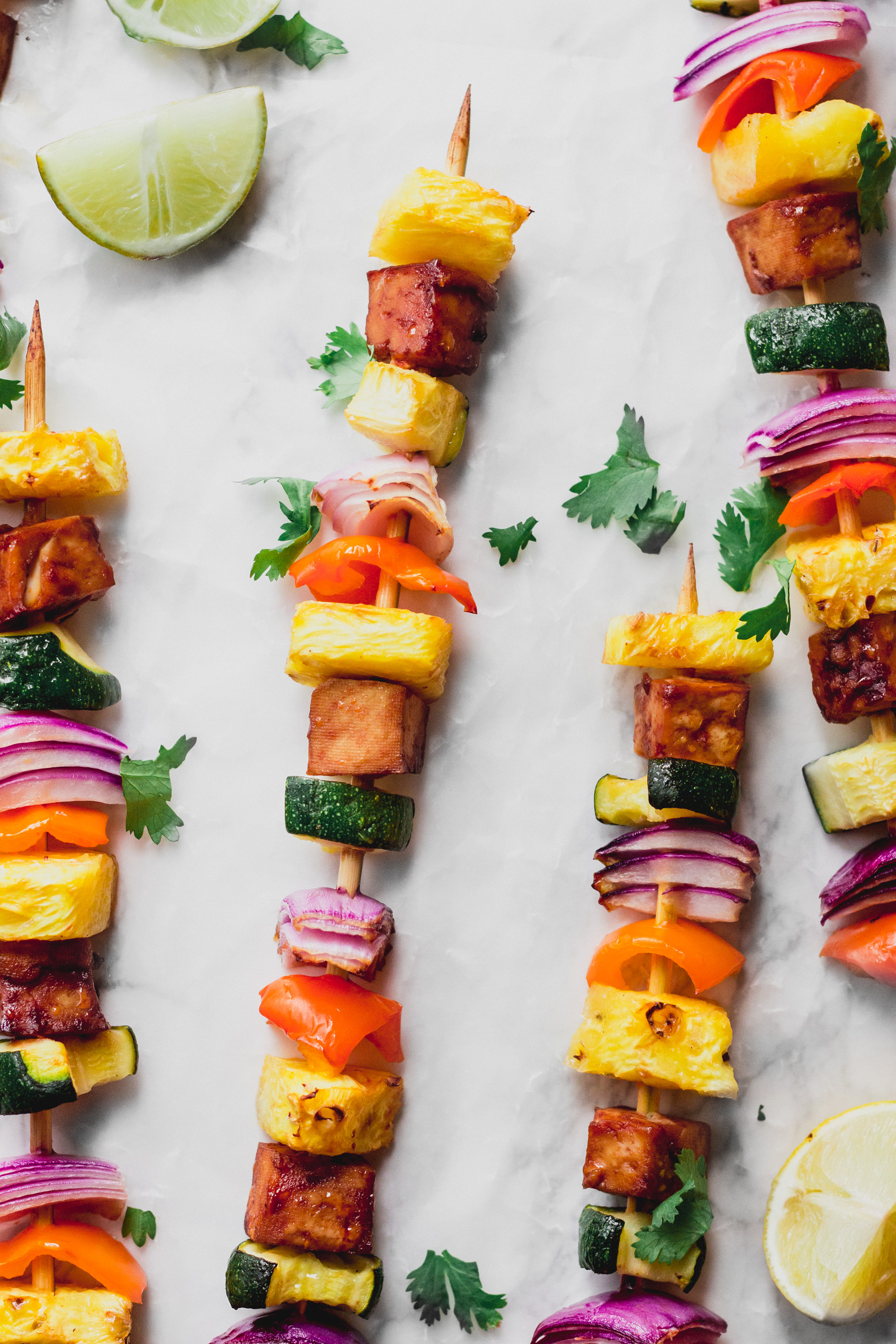 a group of four tofu veggie kebabs served with lime wedges