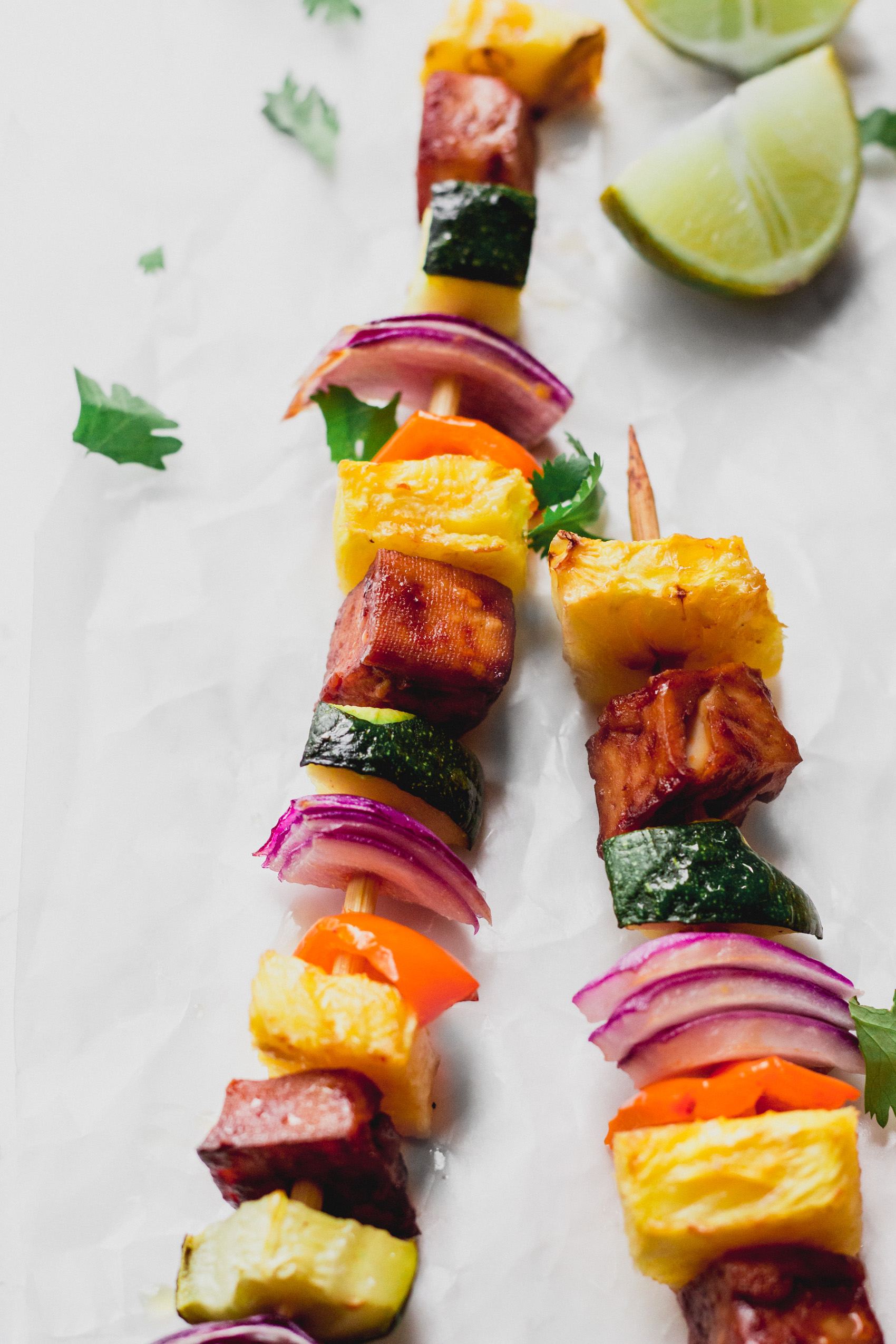 a close up shot of two vegetable skewers each with pineapple, onion, peppers, squash and tofu