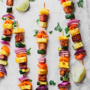 a group of five vegetable kebabs each with pineapple, onion, peppers, squash and tofu