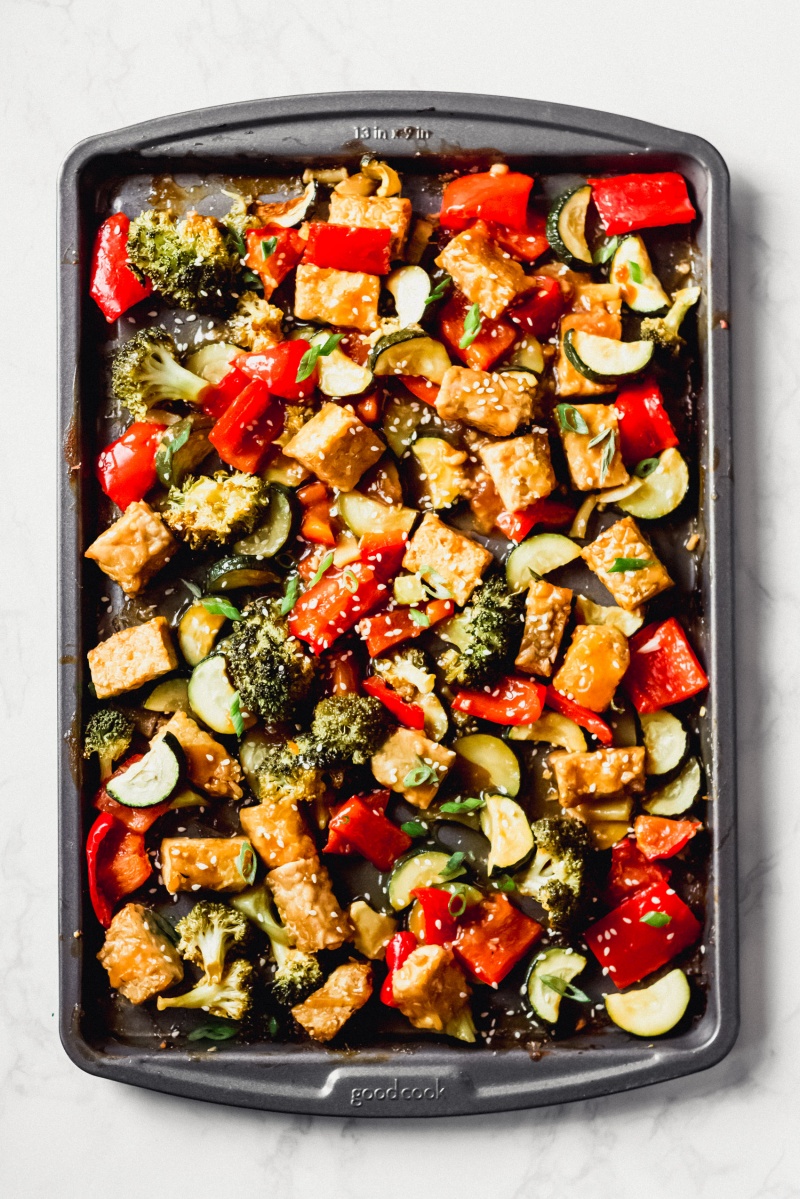 a sheet tray of cooked tempeh and vegetables topped with sesame seeds