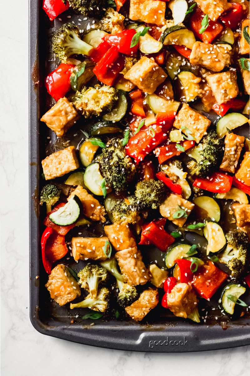 a sheet tray full of roasted tempeh and vegetables topped with sesame seeds