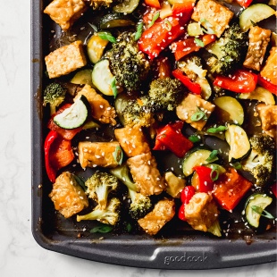 a sheet tray of cubed tempeh and roasted vegetables topped with sesame seeds
