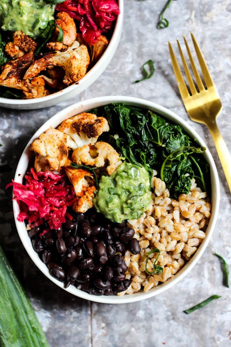 overhead shot of white bowl with rice and black beans with avocado next to a gold fork