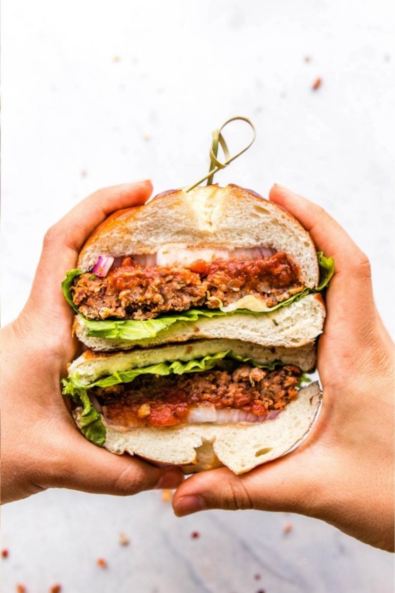 hands holding large vegan pizza burger