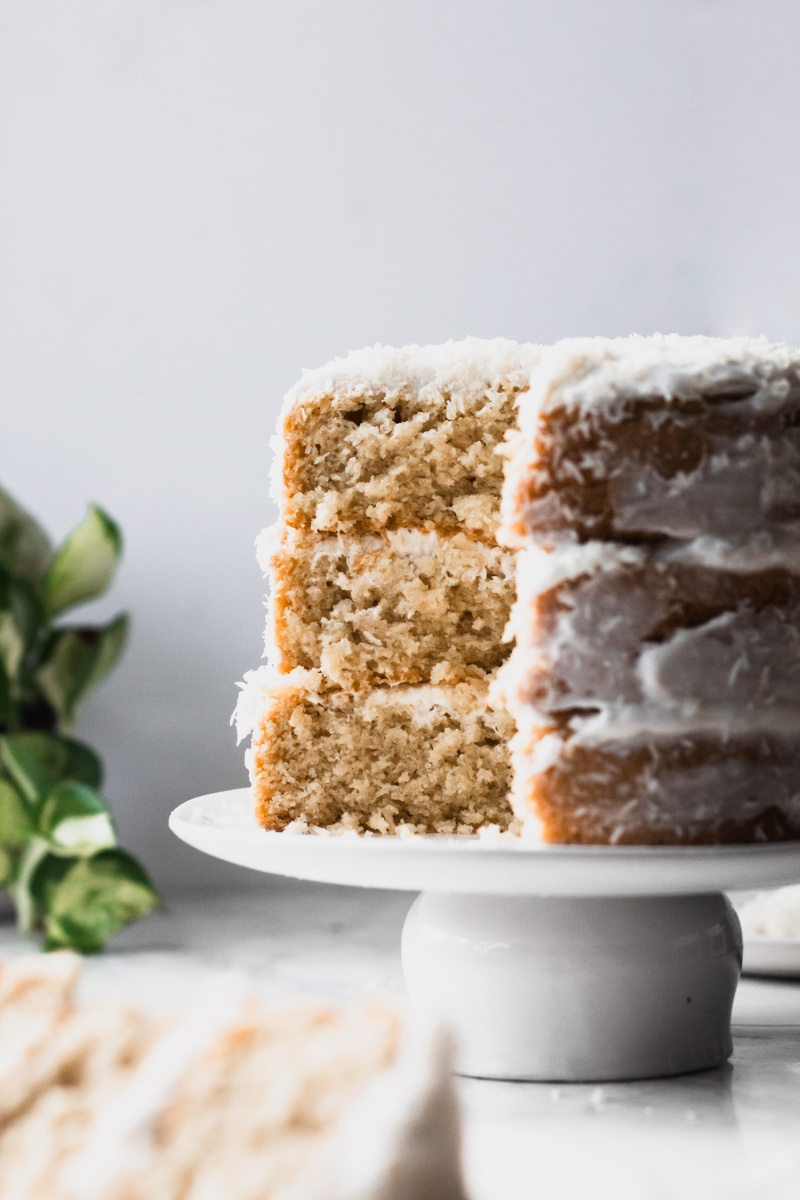 one slice cut out of vegan coconut cake on a white cake stand