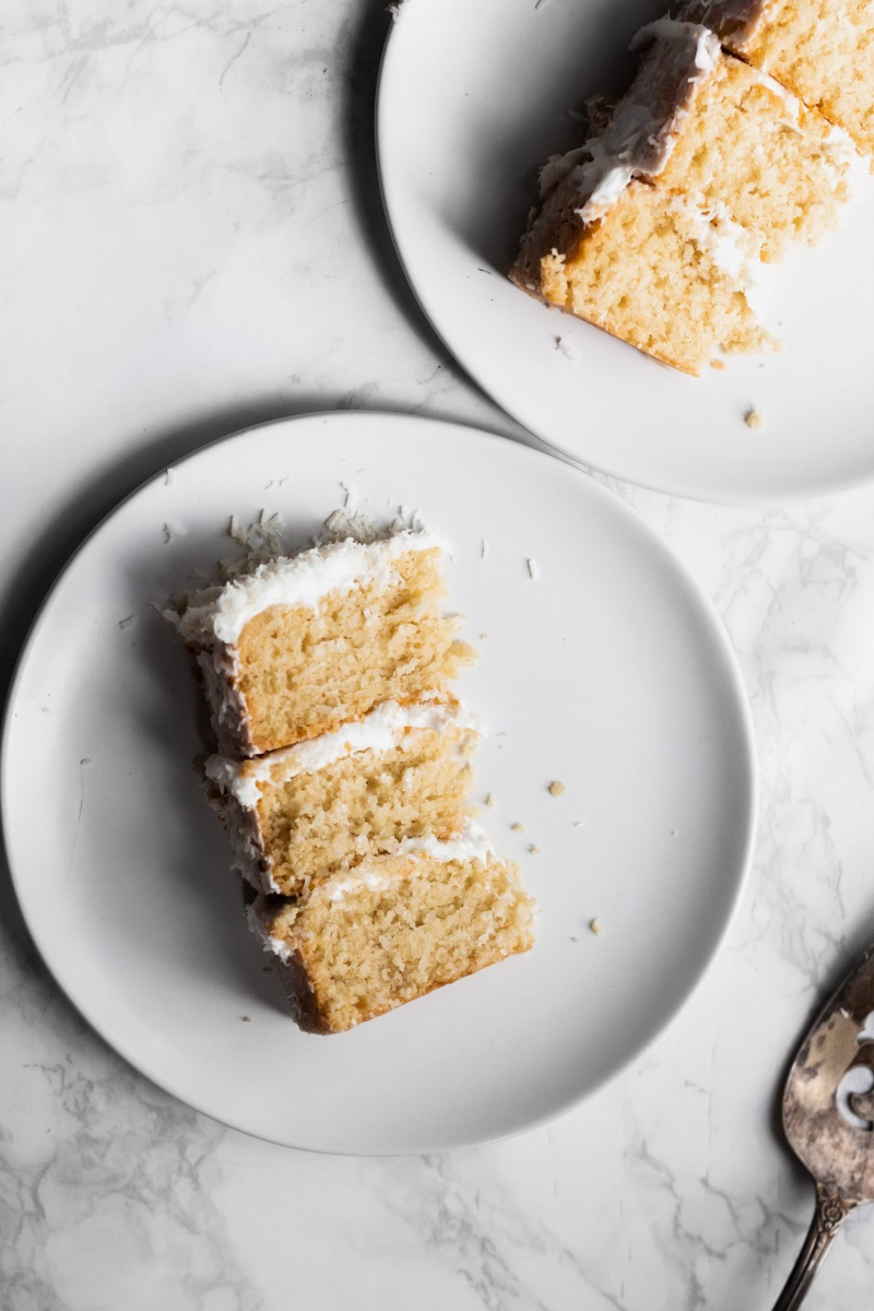 two slices of vegan layer cake on white plates on a marble table