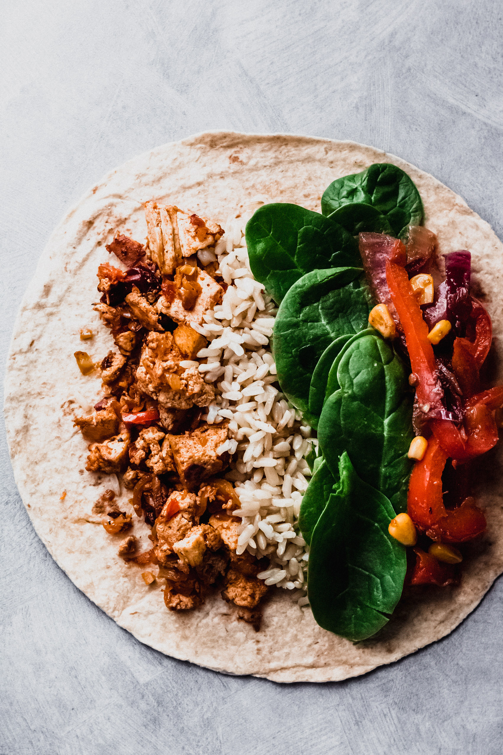 a tortilla filled with tofu, rice, bell pepper and spinach