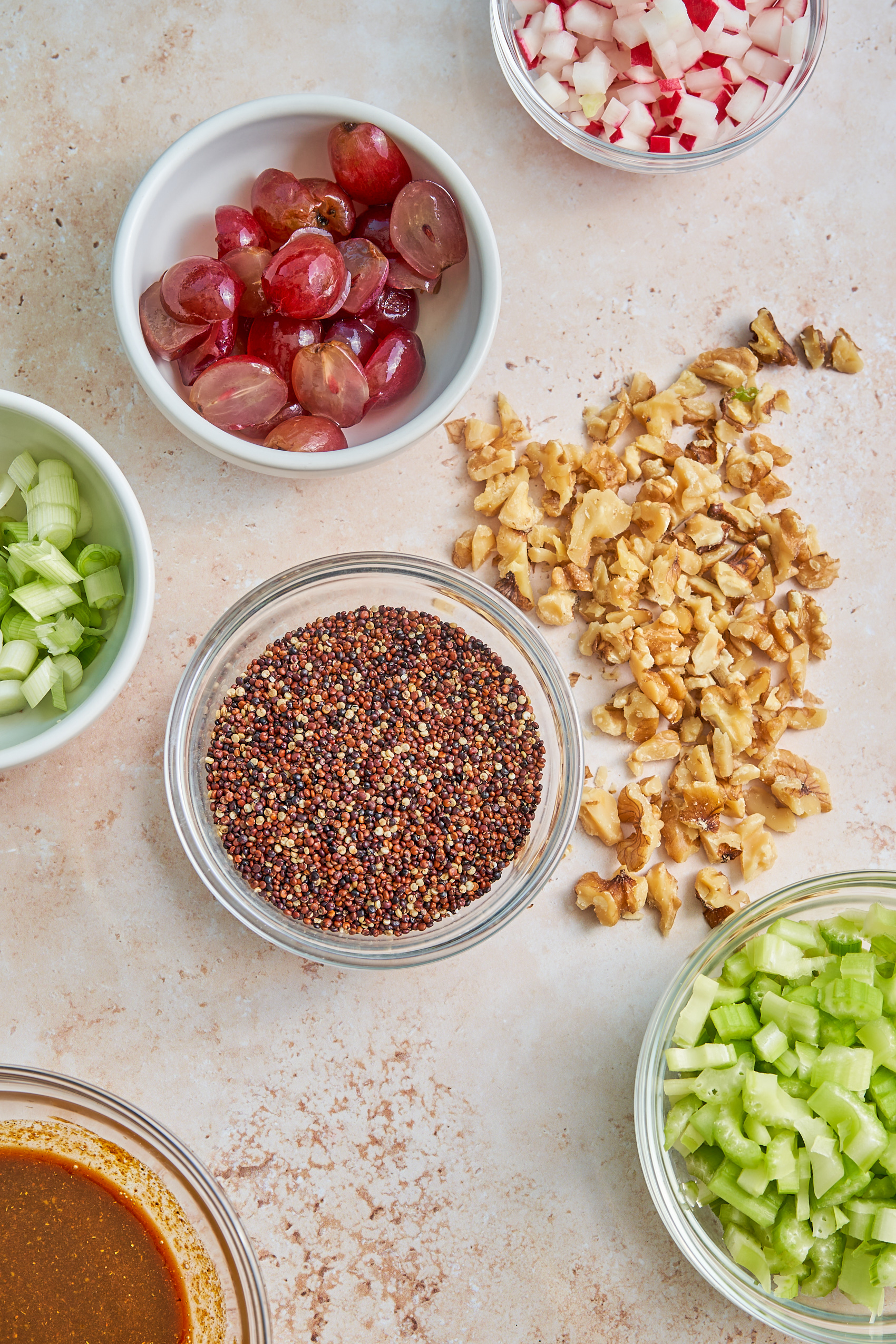 small bowls of ingredients including sliced grapes, chopped celery, green onion, red quinoa and chopped walnuts