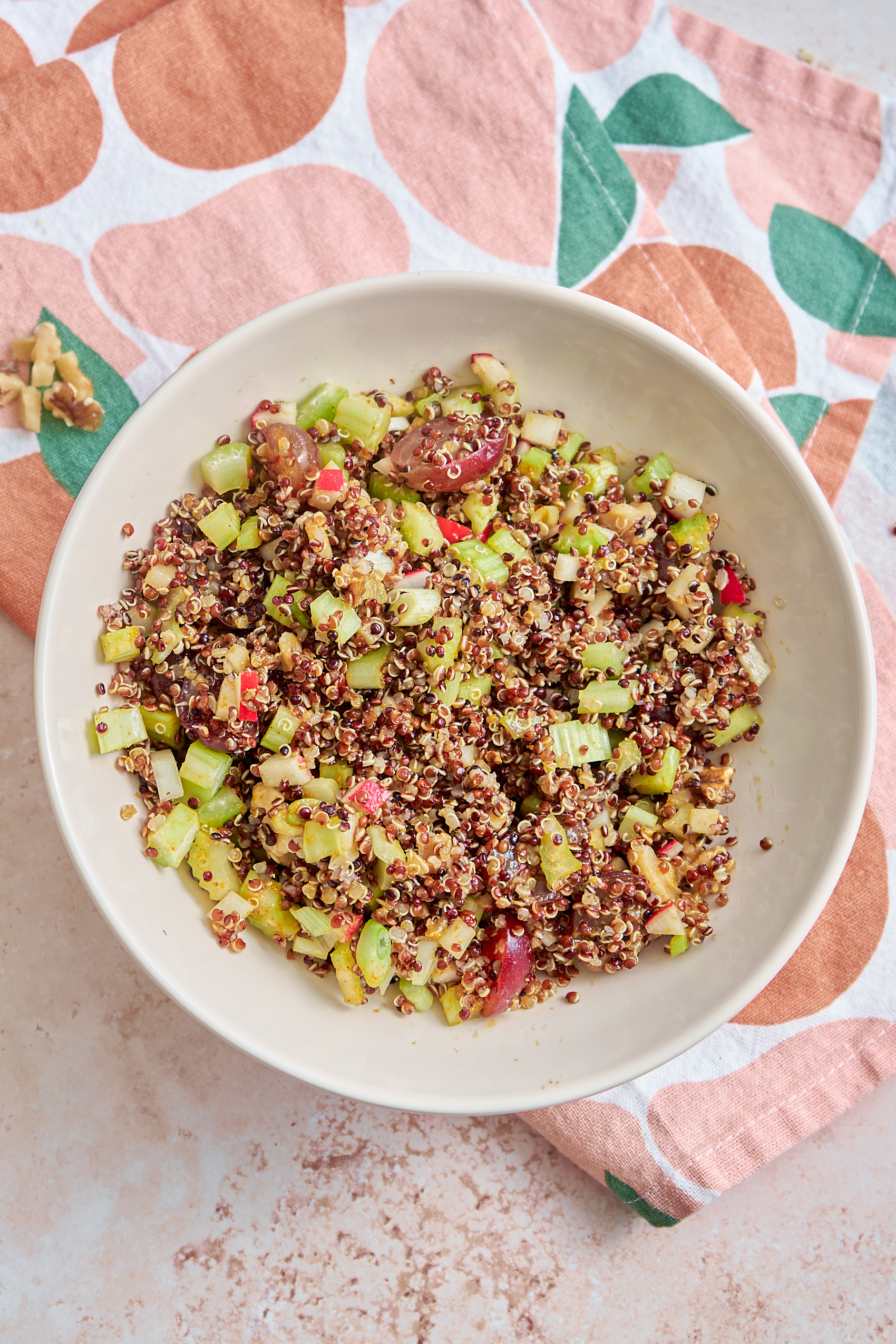 a bowl of quinoa salad containing celery, grapes, walnuts, red quinoa and a curry vinaigrette dressing
