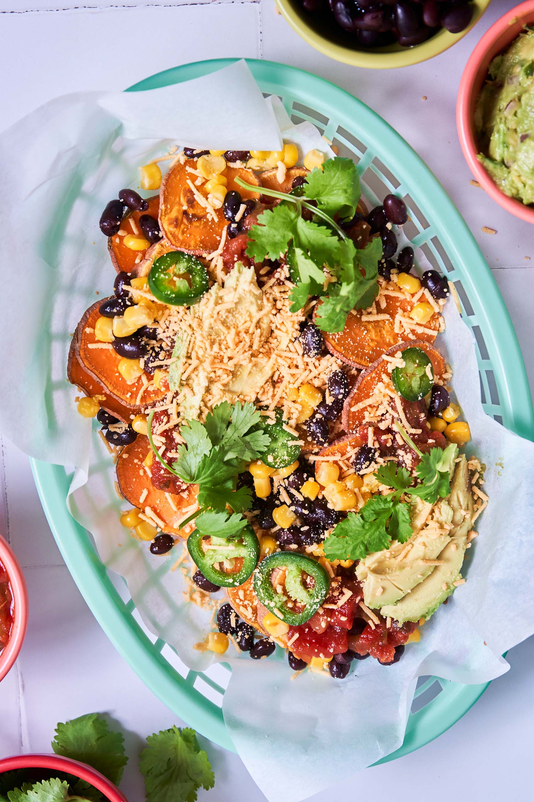 a tray of loaded sweet potato nachos topped with cilantro, sliced jalapenos, cilantro, vegan cheese and black beans