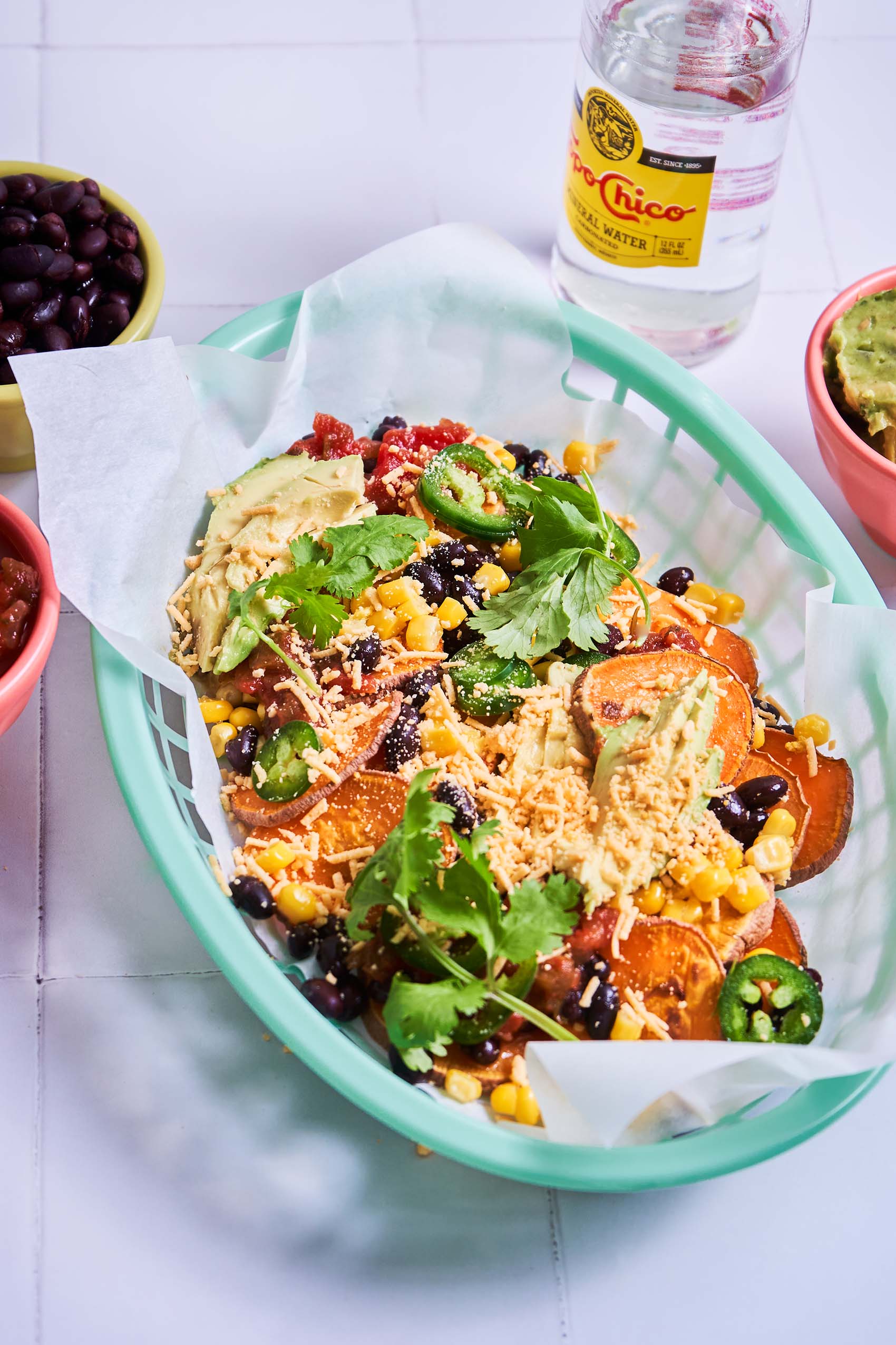 a basket of vegan sweet potato nachos topped with vegan cheese, cilantro, jalapeno, black beans and corn served with guacamole and salsa