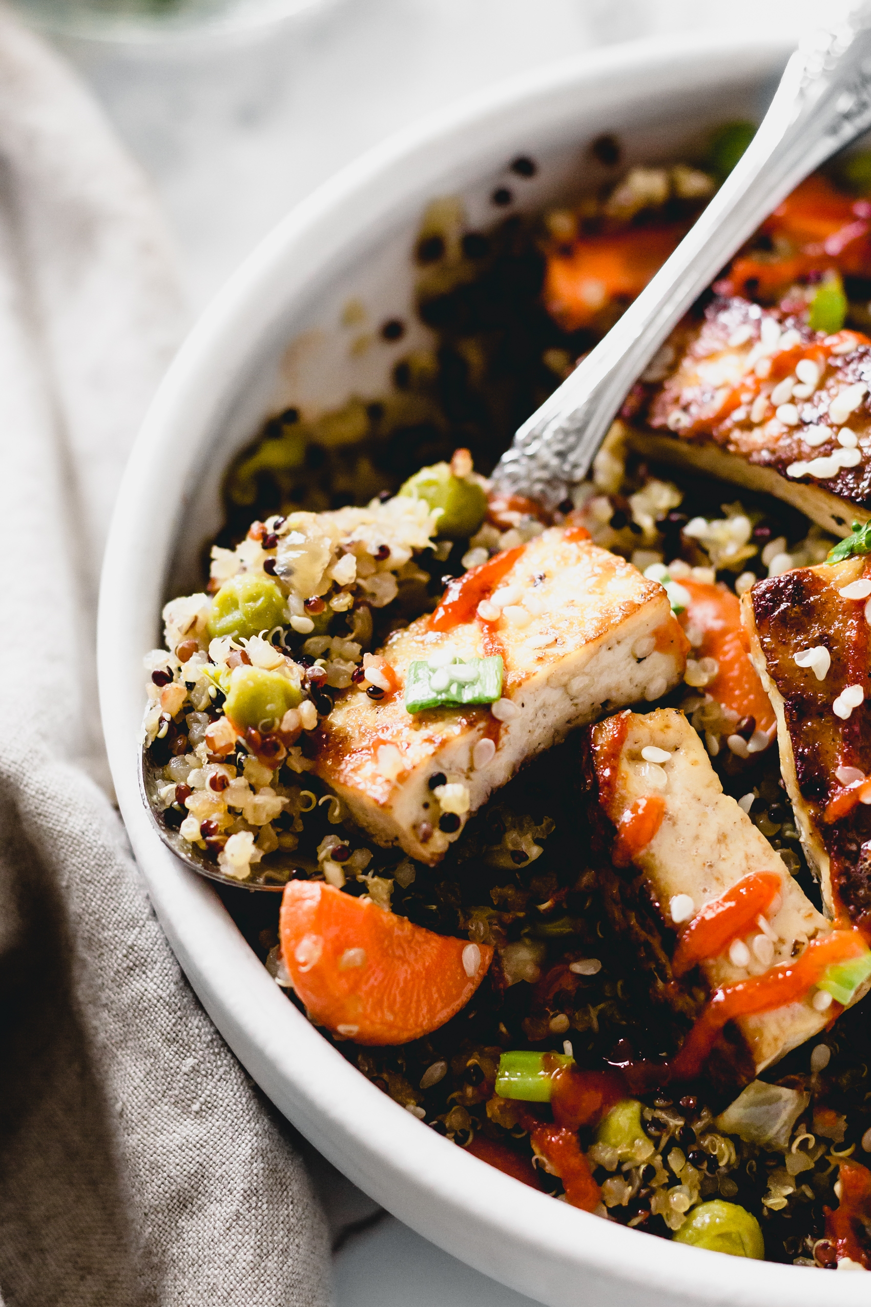 a spoon taking a scoop of stir fried tofu and quinoa