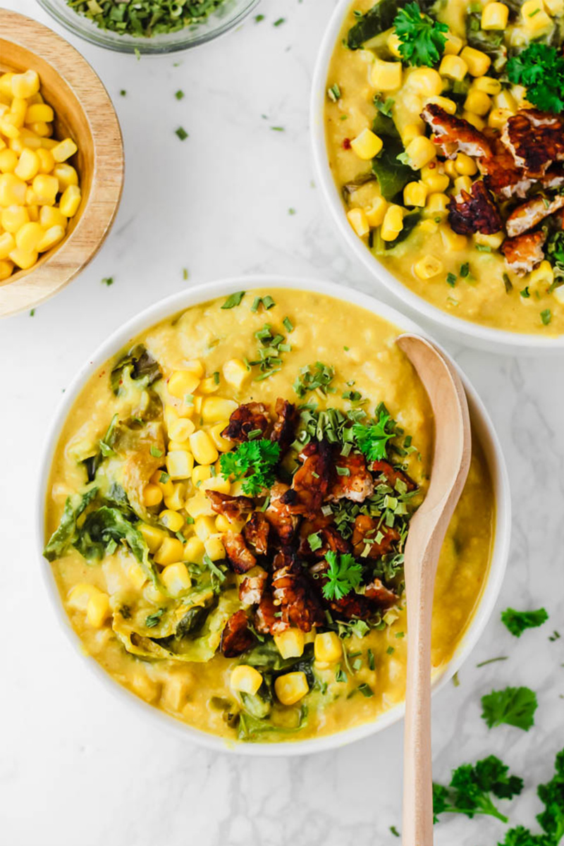 vegan soup with corn and kale in a white bowl on a white table 