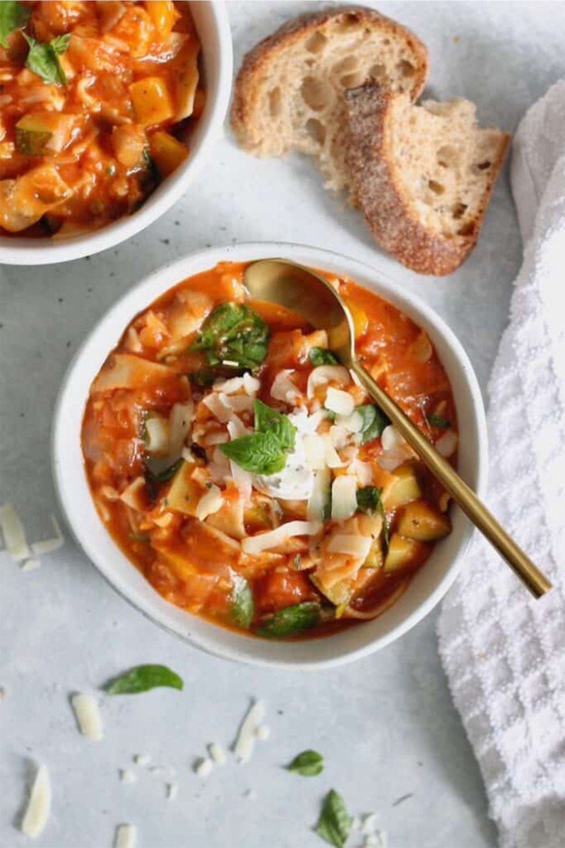 vegan soup with lasagna noodles on a white board next to torn bread