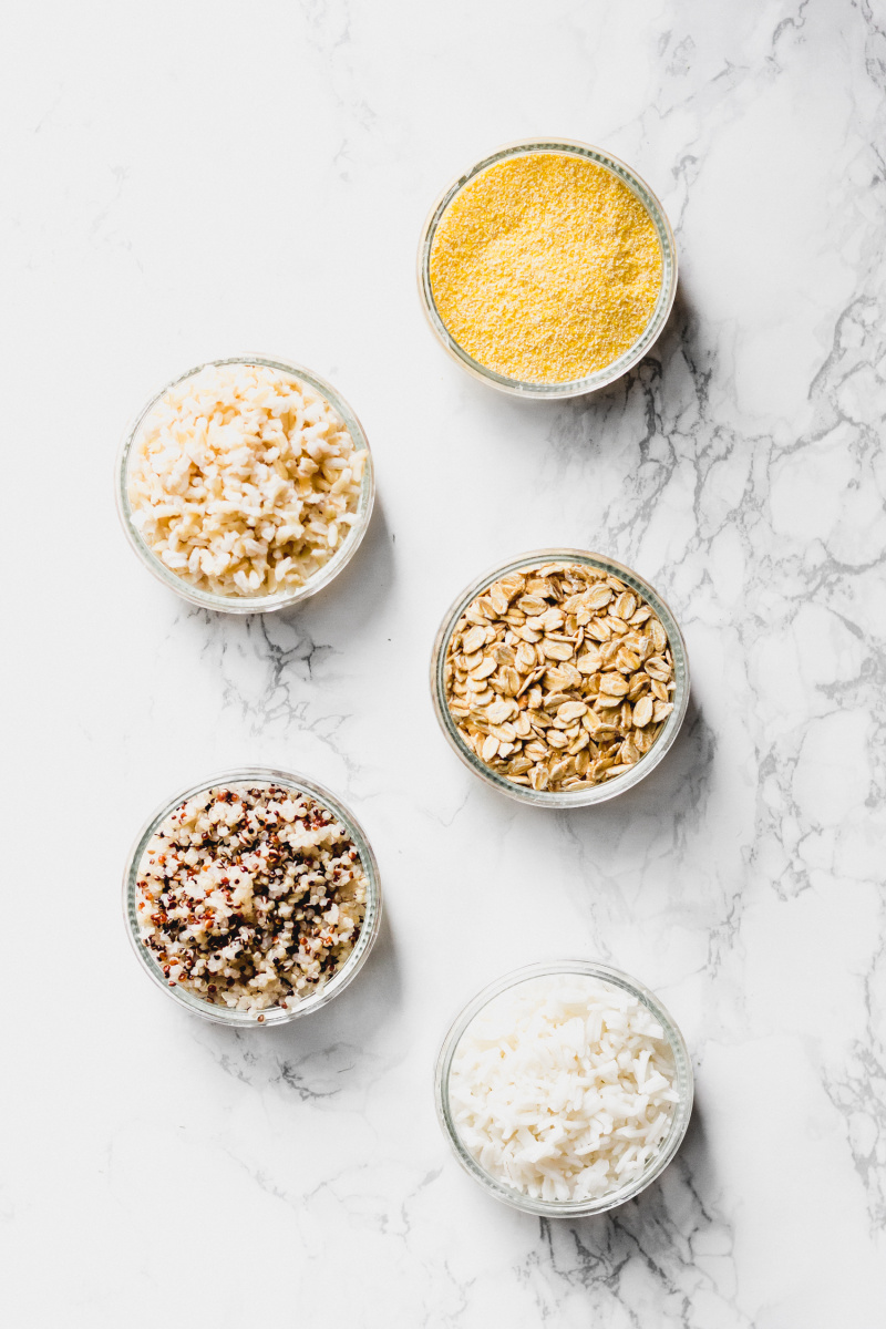 five small bowls filled with various carbohydrate sources including white rice, oats, quinoa, brown rice and cornmeal