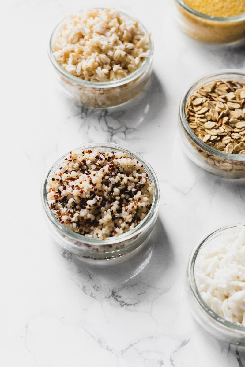 a close up of small dishes of quinoa, brown rice, oats and white rice