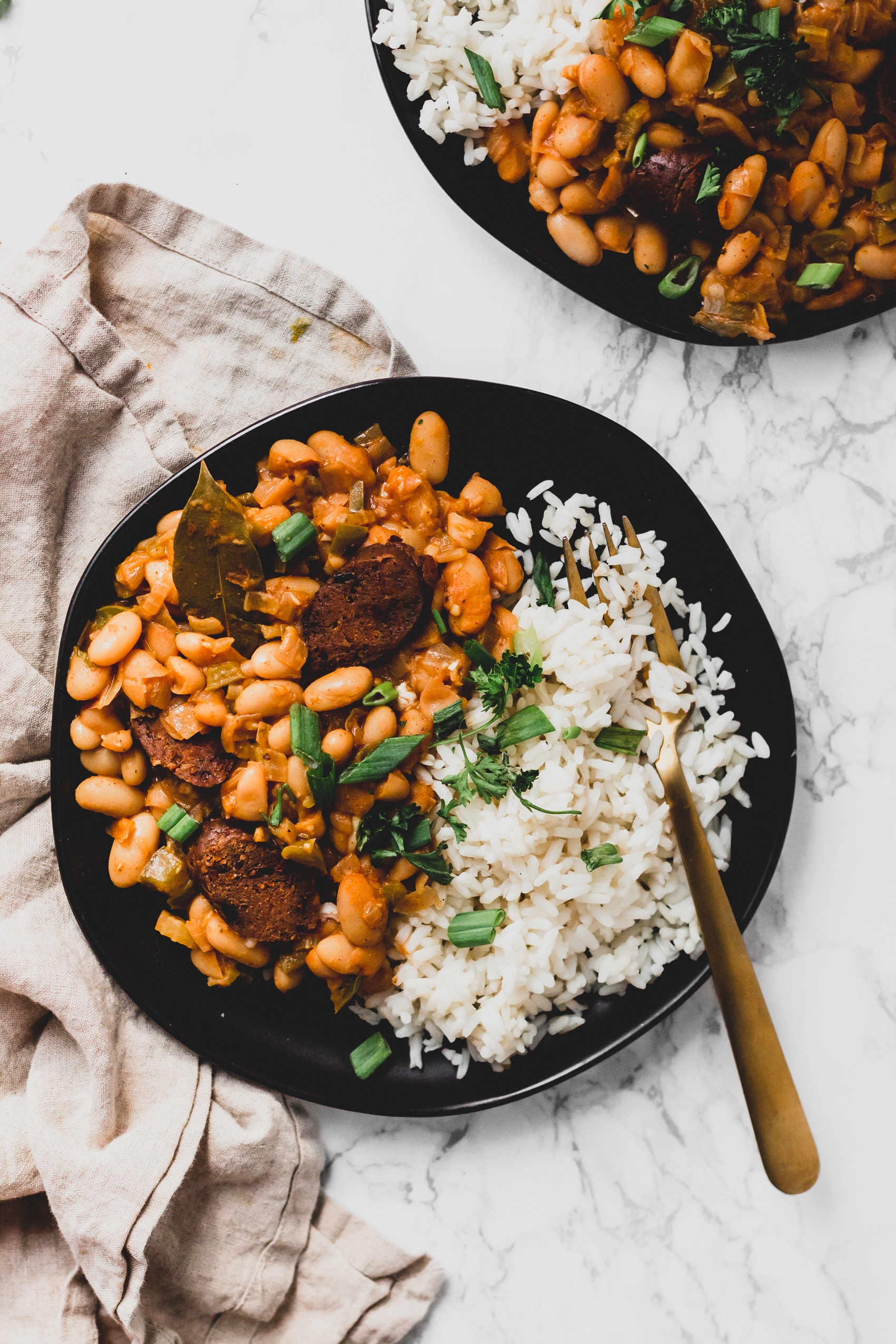 a close up of a plate of cajun white beans served with white rice and fresh parsley