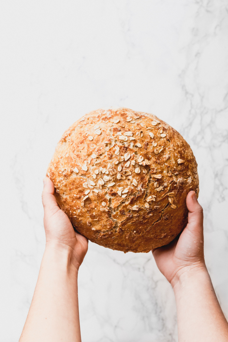 overhead view of two hands holding a round loaf of bread with oats on top