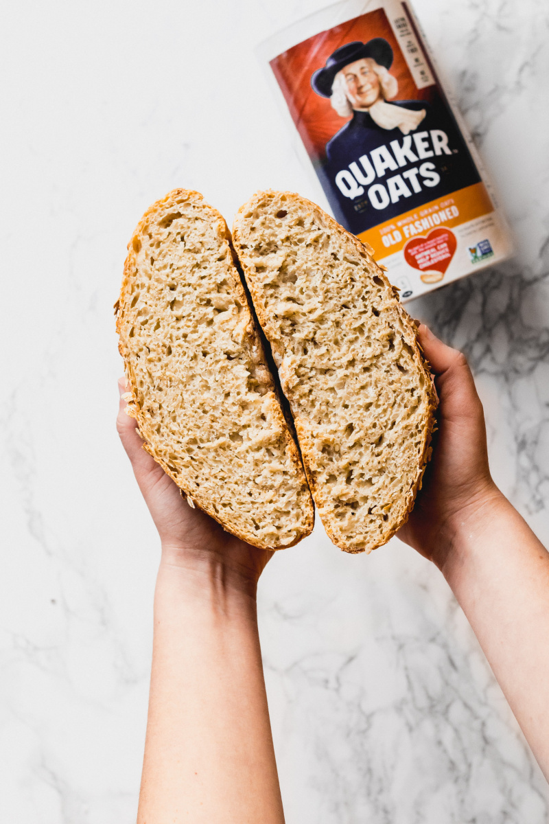 two hands holding two halves of homemade bread with a Quaker oats container