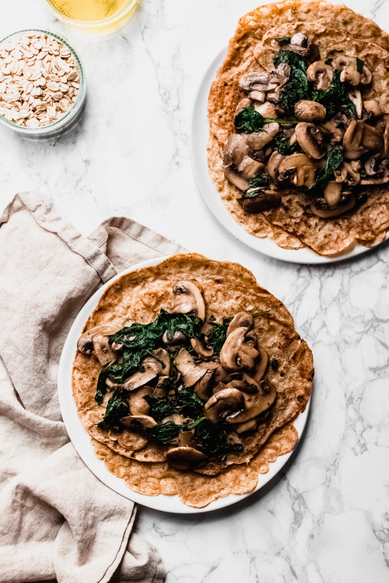 overhead shot of two plates of crepes with mushrooms and spinach on top