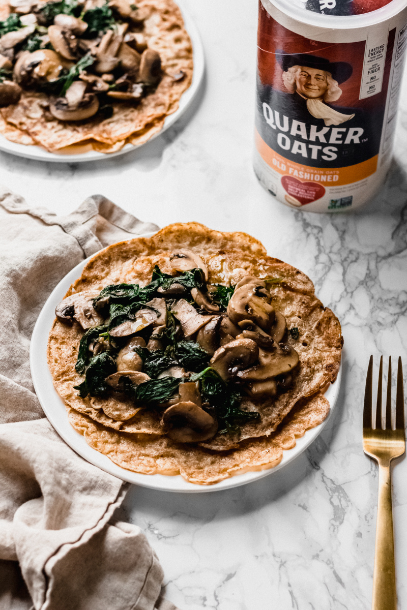 side view of thin pancakes with mushrooms and spinach with a Quaker Oats container next to the plate
