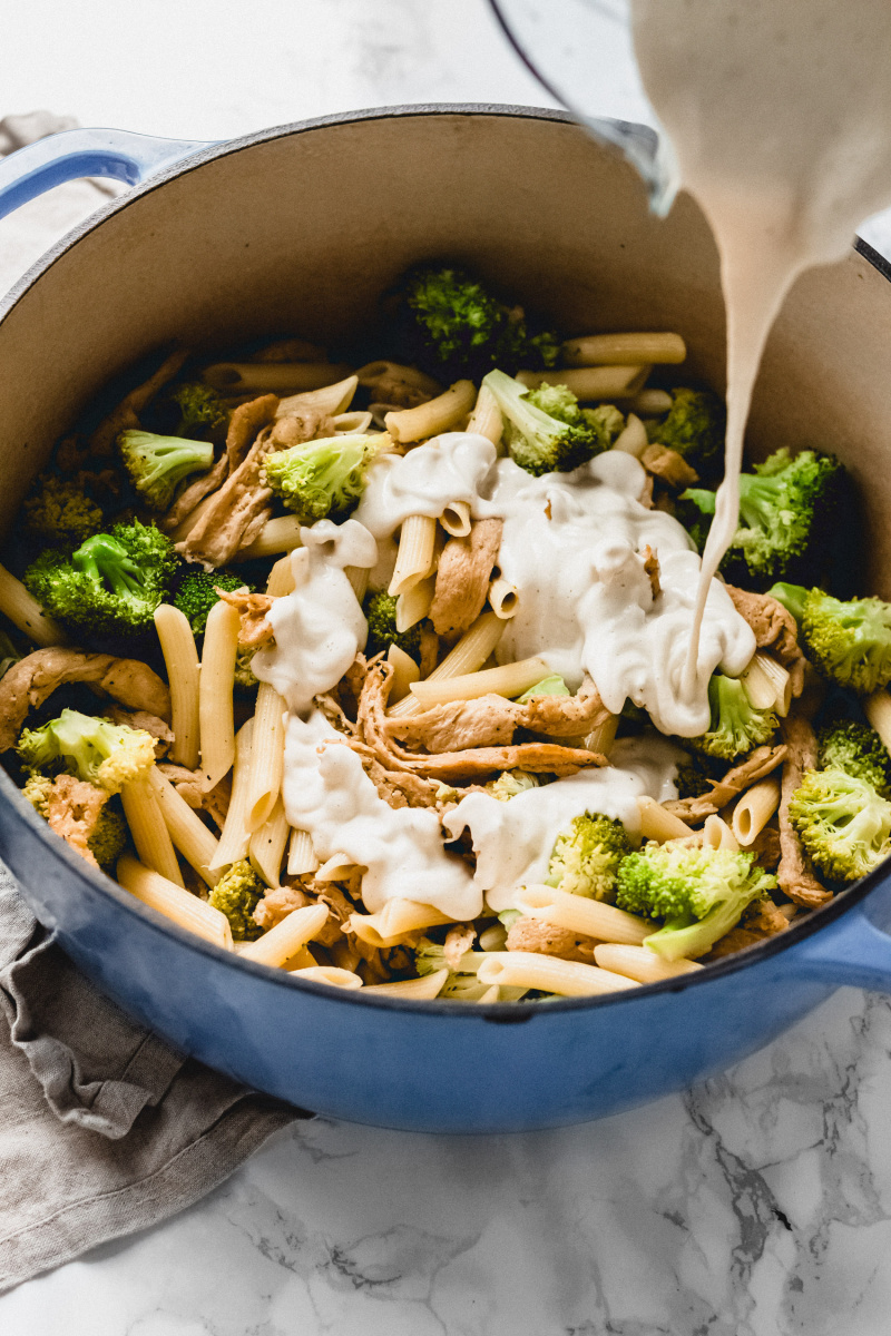 cashew alfredo sauce poured into a pot of pasta and broccoli