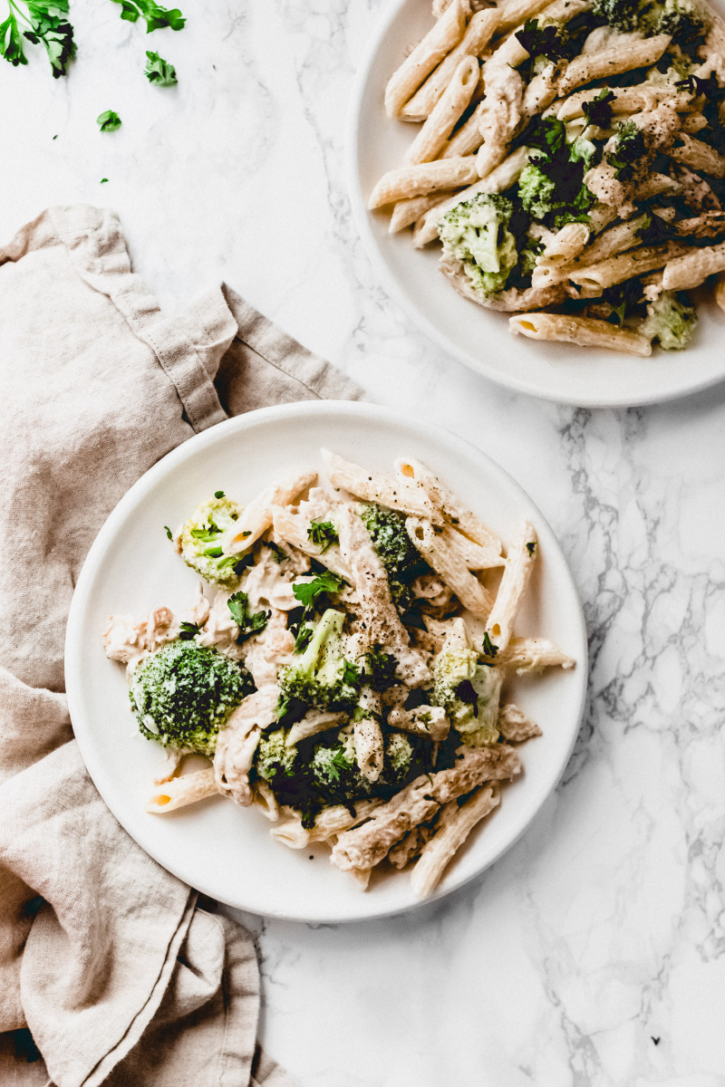 overhead view of two plates of chicken broccoli alfredo with a cloth napkin