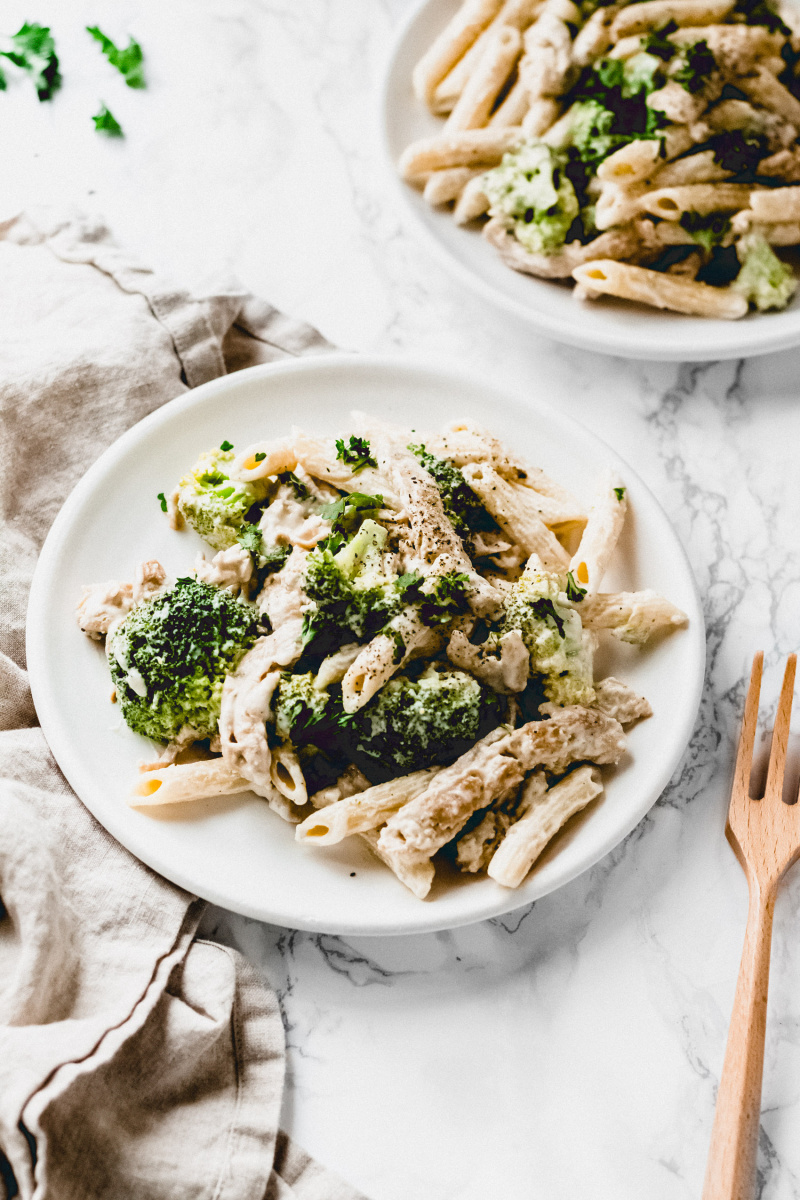 side view of pasta in white sauce with broccoli and a fork