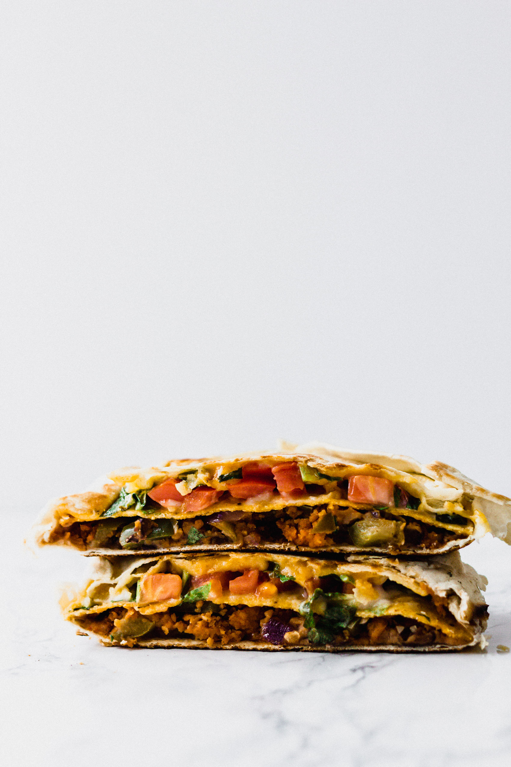 two halves of a tortilla filled with vegan meat, cheese, and vegetables cut in half