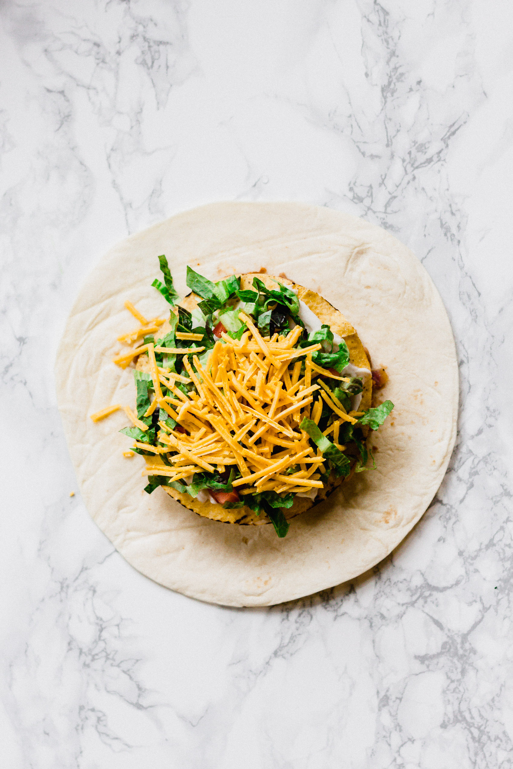 overhead view of a large flour tortilla with lettuce and cheese