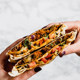 two hands holding a vegan crunchwrap that has been sliced down the middle