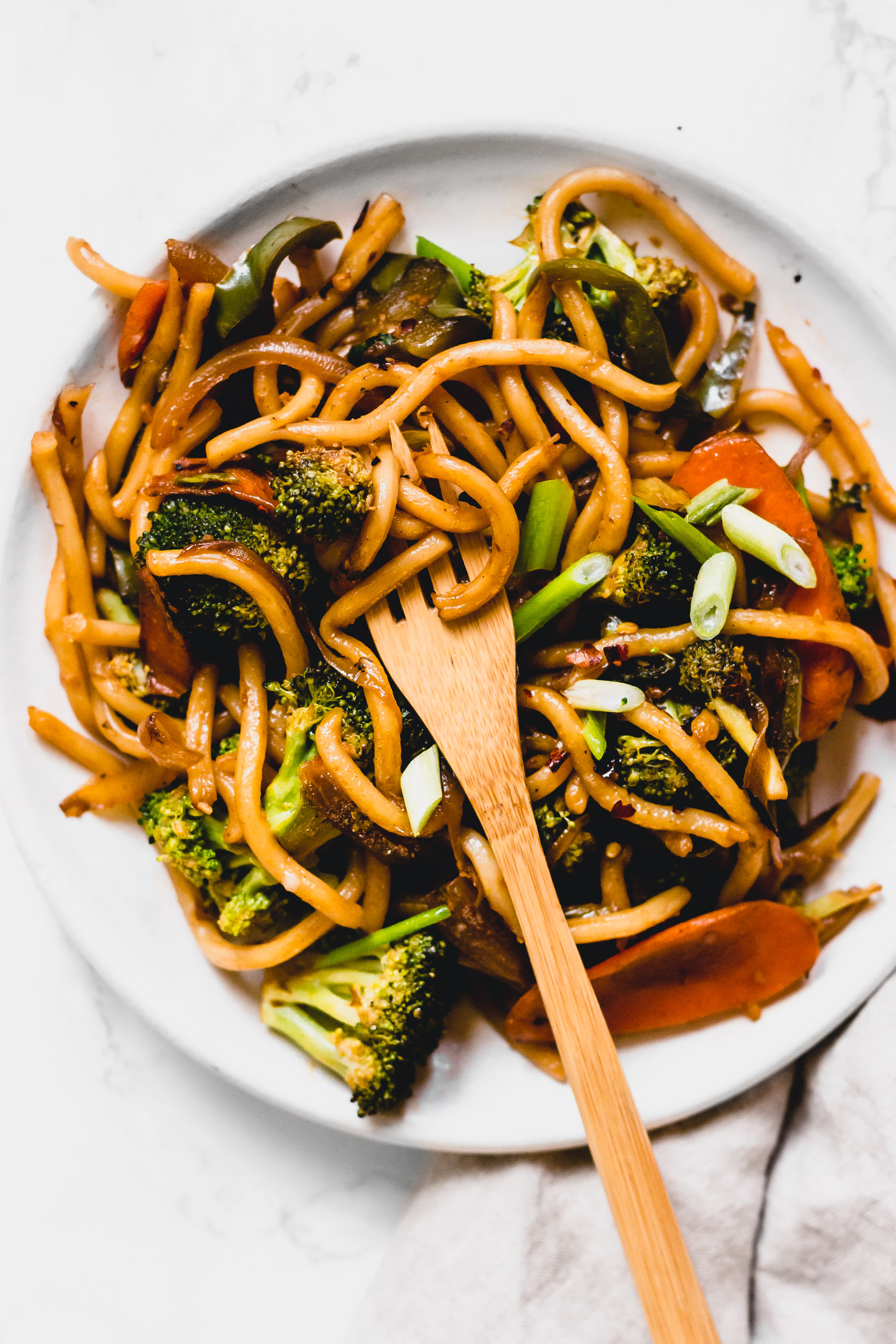 a fork scooping into a plate of vegan stir fried udon noodles