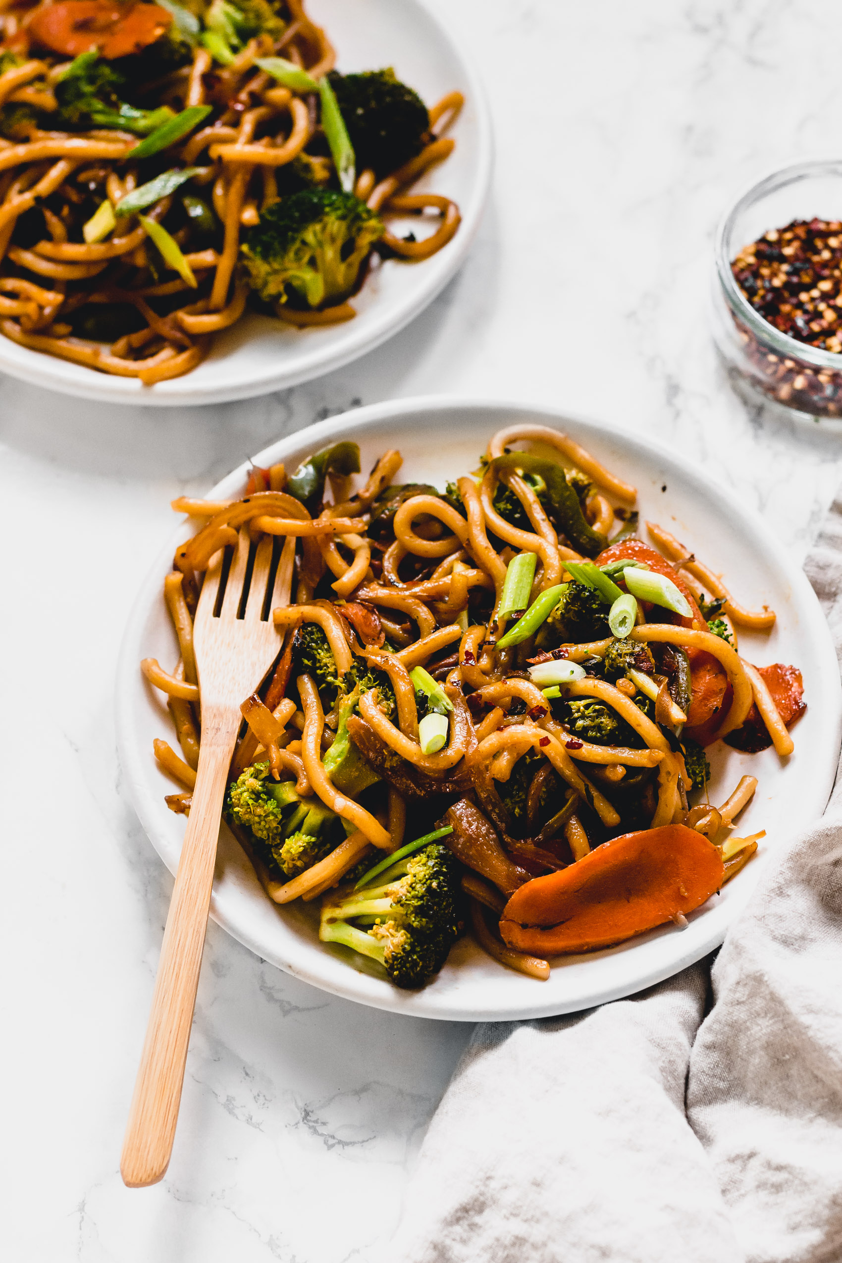 a fork digging into a plate of vegan udon noodle stir fry