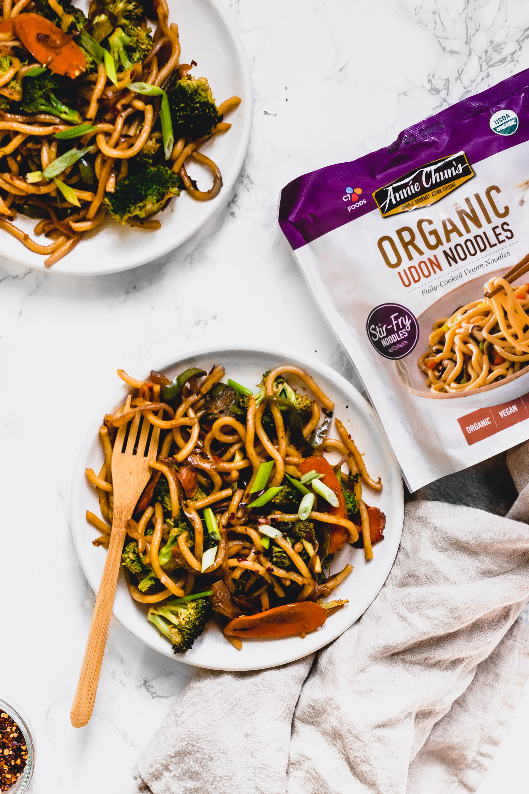 two plates of vegan drunken noodles next to a package of Annie Chun's Organic Udon Noodles