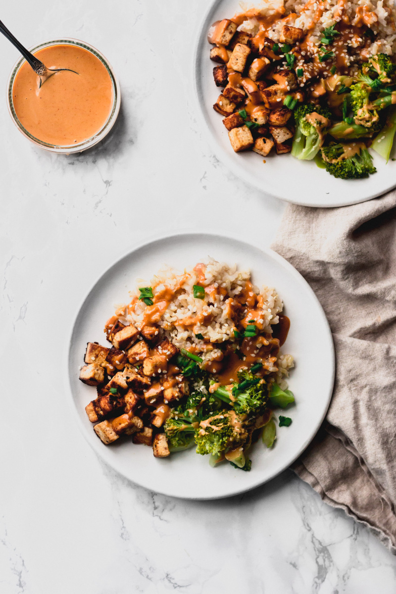 overhead shot of two white plates with tofu and broccoli with peanut sauce