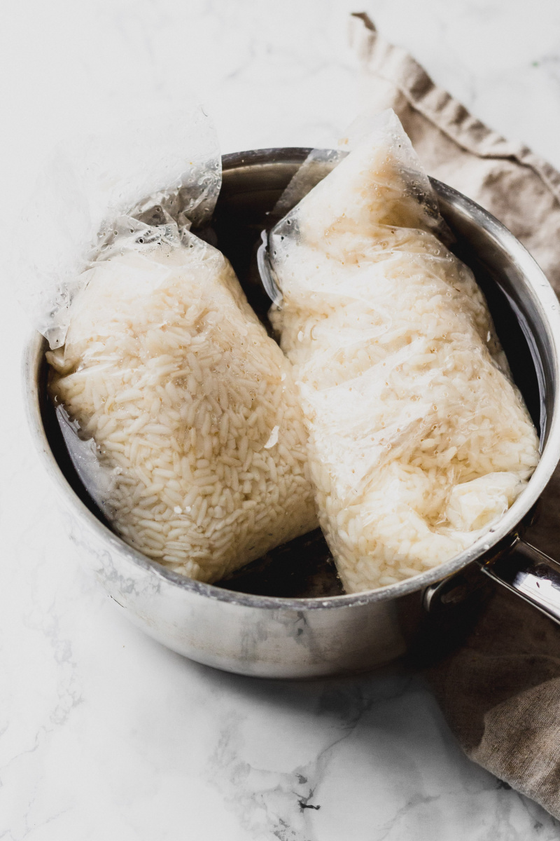 side view of a stainless steel pot with two bags of white rice in water